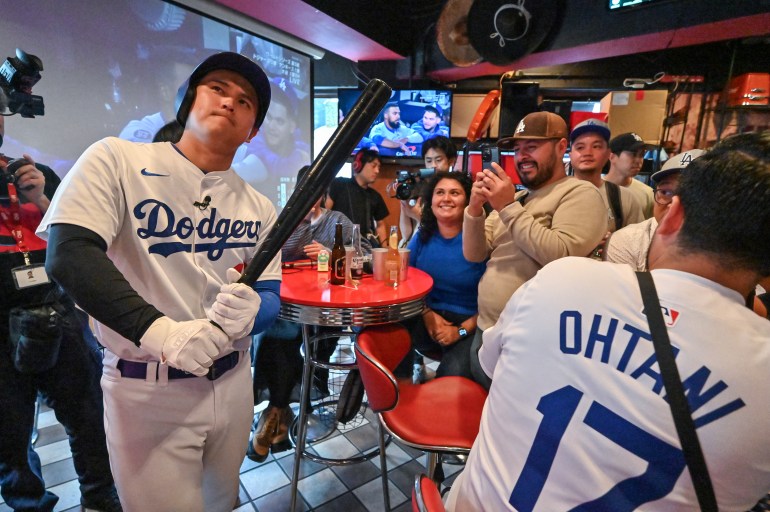 A Shohei Ohtani impersonator (L) poses with a bat at a bar in Tokyo's Shibuya district on October 31, 2024, during a live broadcast of Game 5 of the US Major League Baseball World Series between the Los Angeles Dodgers and New york. Yankees in New York. (Photo by Richard A. Brooks / AFP)